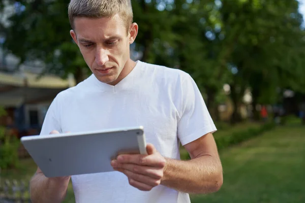 Mladý pohledný muž stojící na ulici a hledající něco na svém tabletu — Stock fotografie