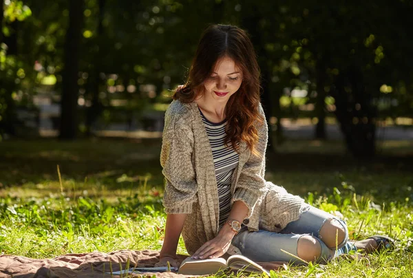 Genç bir kadın sessiz yeşil çimenlerde oturuyor ve kitap okuyor. — Stok fotoğraf