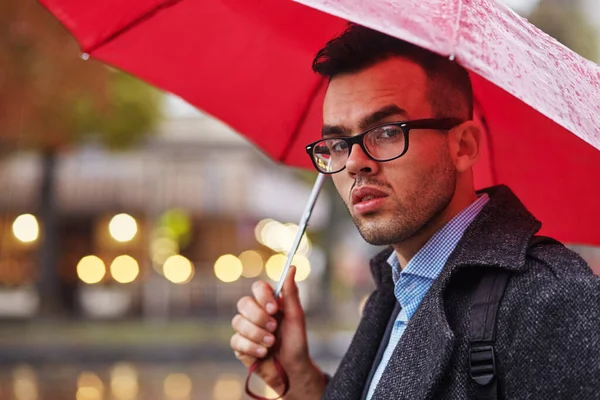 İş adamı yağmurda kırmızı şemsiyeyle gider. Stok Resim