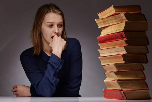 Uma jovem e muitos livros ao lado dela. ela tem dificuldade em aprender — Fotografia de Stock