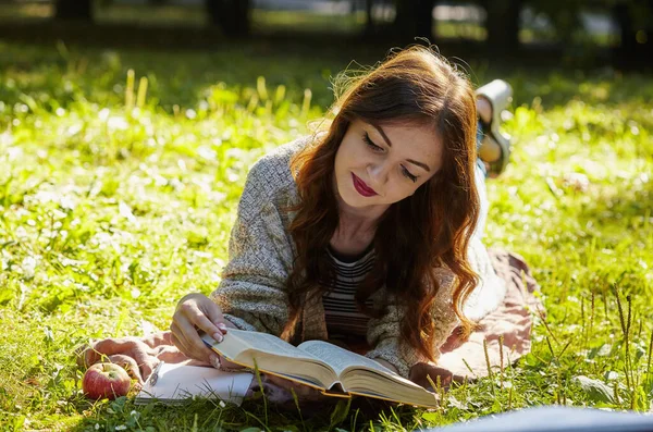 Schöne Frau, die im grünen Gras liegt und an einem Sommertag ein Buch liest — Stockfoto