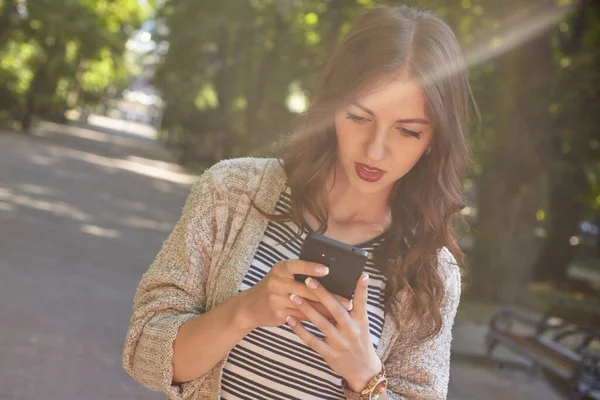 Hermosa mujer va al parque con smartphone y lee noticias —  Fotos de Stock