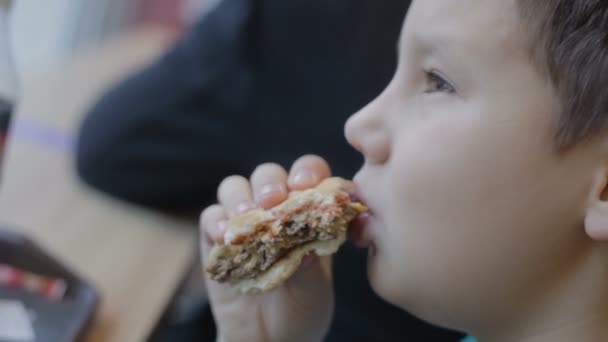 空腹のティーンエイジャーはジャンクフードを食べる。接近中だ。バーガーチーズバーガーサンドイッチ — ストック動画