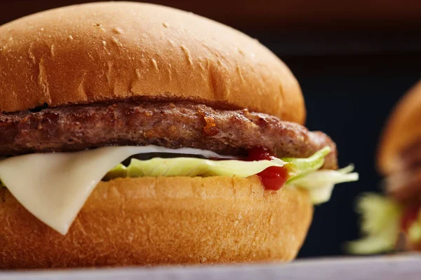 Close-up van heerlijke verse zelfgemaakte hamburger met sla, kaas, ui en tomaat op een rustieke houten plank op een donkere achtergrond. — Stockfoto