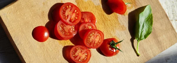 Tomate vermelho em uma tábua de corte com folhas de manjericão no fundo de madeira — Fotografia de Stock