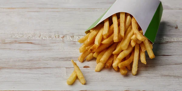 Patatine fritte in un involucro di carta su sfondo di legno . — Foto Stock