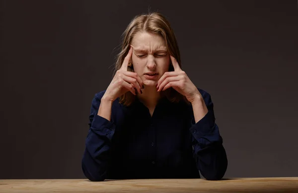 Zeer gespannen jonge vrouw aan tafel op een donkere achtergrond. — Stockfoto