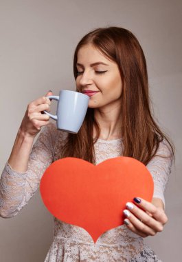 Kız kahve içiyor ve bize kağıttan kesilmiş kırmızı bir kalp gösteriyor.