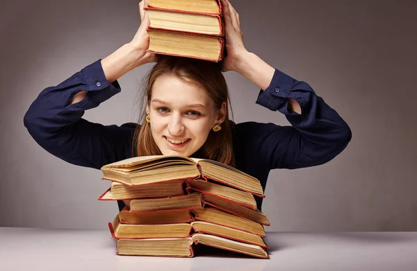 Γυναίκα κάθεται στο τραπέζι και κρατά ένα βιβλίο πάνω από το κεφάλι της σε ένα σκοτεινό φόντο. Η έννοια της μάθησης. — Φωτογραφία Αρχείου