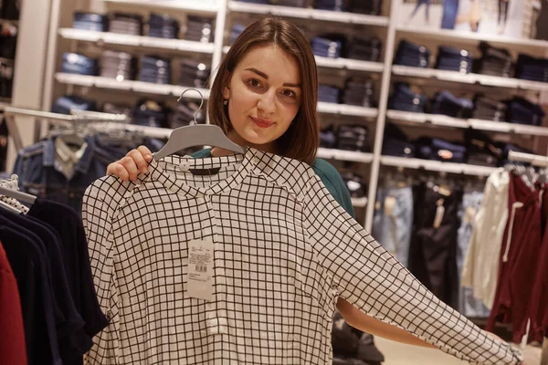Sale, consumentisme en people concept - gelukkige jonge vrouw die kleding kiest in kledingwinkel. — Stockfoto