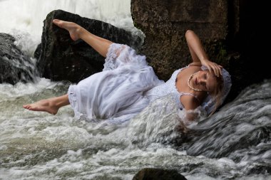 sarışın genç kadın beyaz bir gelinlikle şelalenin yakınında