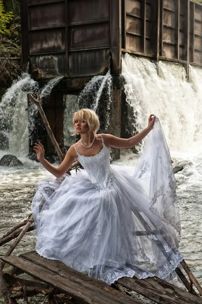 滝のそばの白いウェディング ドレスの若いブロンドの女性 — ストック写真