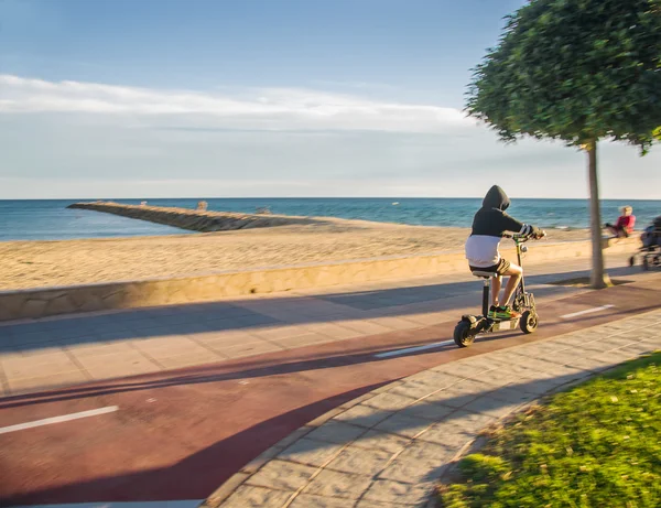 Giovane uomo guida scooter elettrico lungo la spiaggia di autunno . — Foto Stock