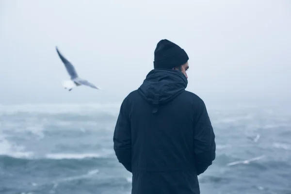 Hombre con un abrigo gris caminando cerca del mar —  Fotos de Stock