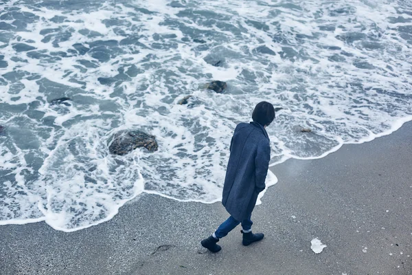 Uomo con un cappotto grigio che cammina vicino al mare — Foto Stock