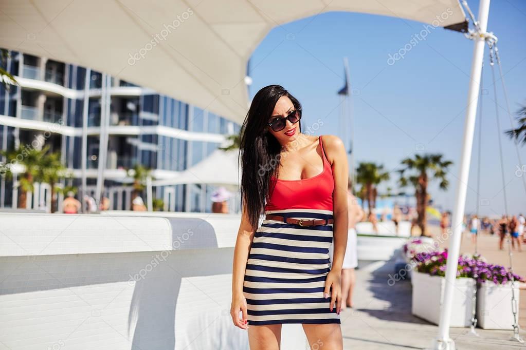 beautiful sexy brunette in tight dress walks along the waterfront on a sunny day