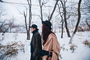 Young hipster beautiful couple in black hats in the winter forest,love,winter vacation in mountains,jeans,warm coat,traveling,hiking,winter walk in love,man in a green coat.girl in a beige coat