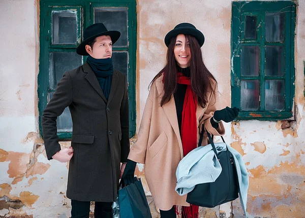 Joven pareja hipster hermosa en sombreros negros en el bosque de invierno, el amor, vacaciones de invierno en las montañas, jeans, abrigo cálido, viajar, senderismo, paseo de invierno en el amor, el hombre con una capa verde.girl en un abrigo beige — Foto de Stock