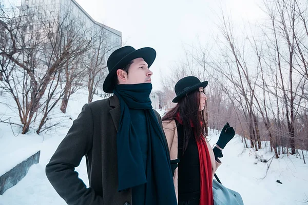 Young hipster beautiful couple in black hats in the winter forest,love,winter vacation in mountains,jeans,warm coat,traveling,hiking,winter walk in love,man in a green coat.girl in a beige coat — Stockfoto