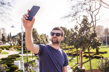 Yakışıklı adam selfie park.man kullanım telefon, akıllı telefon, şık adam ile smartphone kullanarak güneş gözlüğü içinde alarak