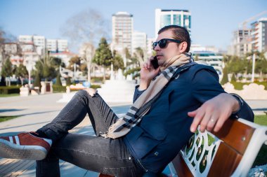 Yakışıklı adam telefon vasıl belgili tanımlık park. Konuşarak telefon, adam kullanım telefon, şık adam akıllı telefon kullanarak güneş gözlüklü adam