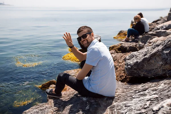 Junger Mann mit Sonnenbrille sitzt auf Felsen — Stockfoto