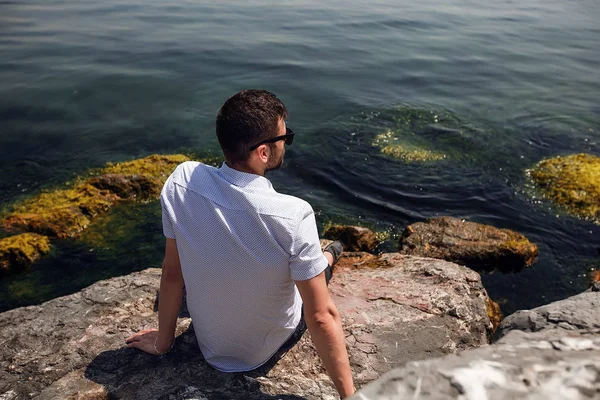 Jeune homme en lunettes de soleil assis sur des rochers — Photo