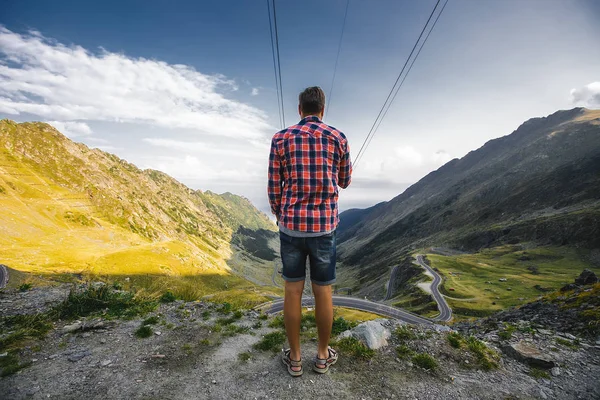 back view of man standing on beautiful serpentine road and mountains background