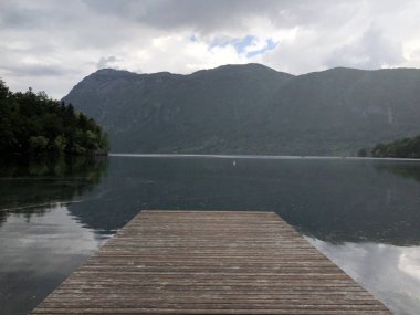 Gündüz vakti ormanla kaplı dağların arasında göldeki ahşap iskele manzarası. 