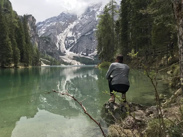 Visão Traseira Viajante Masculino Sentado Costa Lago Entre Montanhas Cobertas — Fotografia de Stock
