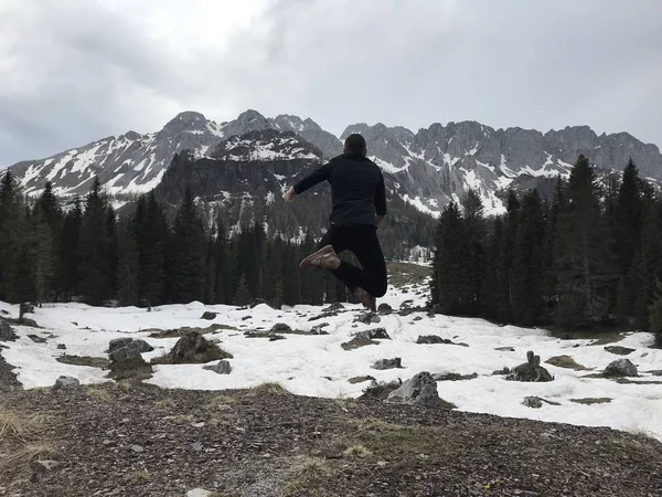 Visão Traseira Viajante Masculino Saltando Entre Montanhas Nevadas Cobertas Floresta — Fotografia de Stock