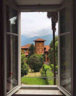 Güzel eski binanın penceresinden manzara ve arka planda dağlar olan yeşil bahçe 