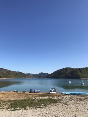 Gündüz vakti ormanla kaplı dağların arasında kıyıdaki ve göl manzaralı tekneler.  