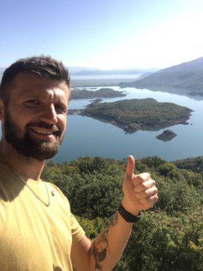 portrait of bearded man showing thumb up and looking at camera with -large river on background 