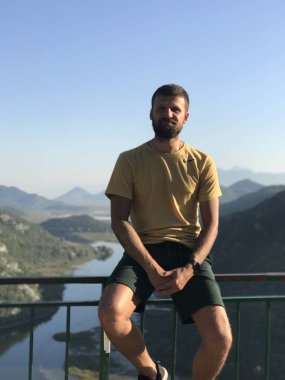 Gündüz vakti ormanla kaplı dağların arasında köprü çitlerinde oturan adam. 