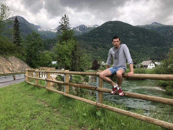 Man Sitting Bridge Fence River Mountains Covered Forest Daytime — Stock Photo, Image