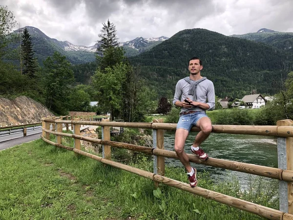 Man Sitter Bro Staket Nära Floden Bland Berg Täckt Med — Stockfoto