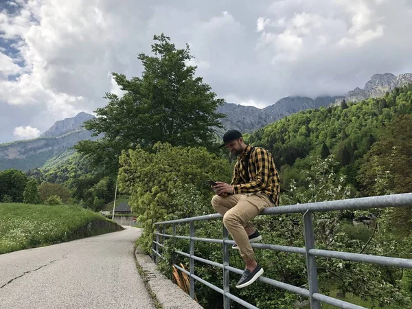Άνθρωπος Κάθεται Φράχτη Γέφυρα Και Χρήση Smartphone Μεταξύ Των Βουνών — Φωτογραφία Αρχείου