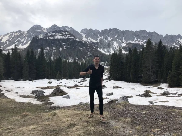 male traveler posing among snowy mountains covered with forest at daytime