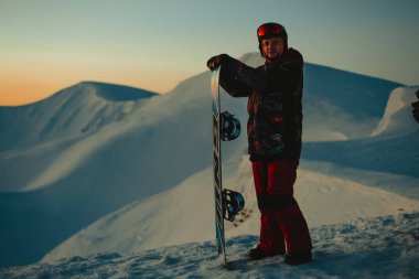 Snowboard yapan ve kış dağlarında tepede duran erkek snowboardcu. 