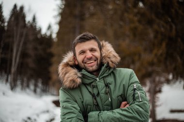 young bearded man in warm coat standing in snow-covered winter forest 