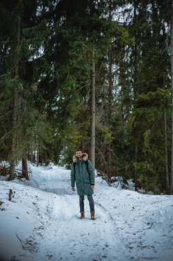 young bearded man in warm coat standing in snow-covered winter forest 