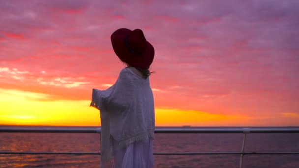 白いドレスとすばらしい夕日で海の背景にポーズの帽子を身に着けている若い魅力的な女性 — ストック動画