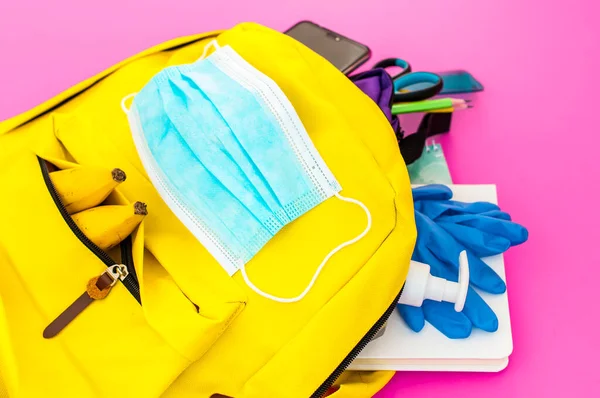 黄色背包 装满了学校必备的工具 还配有面罩 酒精水凝胶和乳胶手套 以防止粉红底色的鳕鱼 图库照片