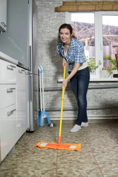 A young woman sweeping the floor, a housewife tidying up in the kitchen