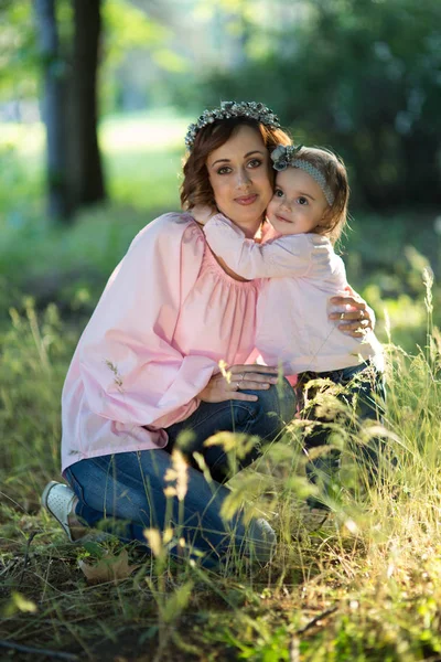 Mom and daughter are two years old sitting on the grass in the p