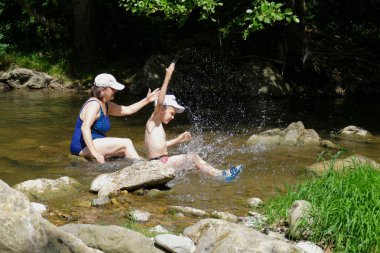 Isı soğutma. Büyükanne ve torunu ile bir dağ dere içinde su sıçramasına.