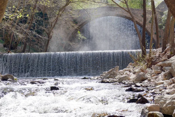 Şelaleli bir nehrin üzerinde eski bir köprü.