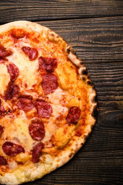 Sıcak pizza dilimi, erimiş peynirle ahşap bir masada..