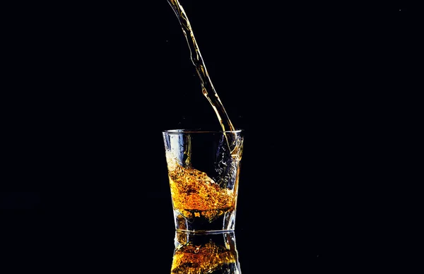 Isolated shot of whiskey with splash on black background, brandy in a glass